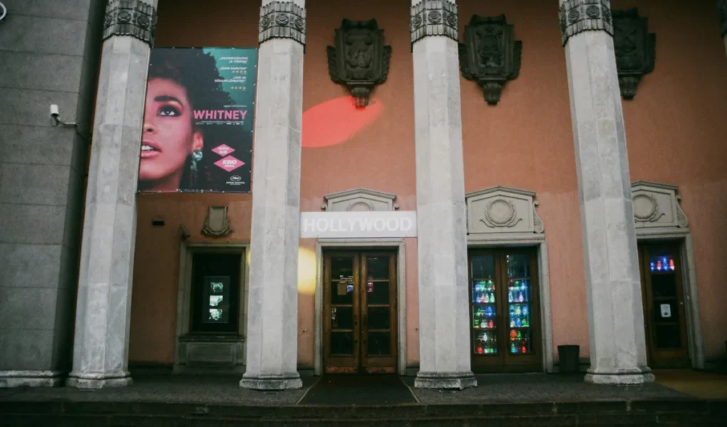Exterior view of a vintage theatre entrance with tall pillars and a colorful poster.