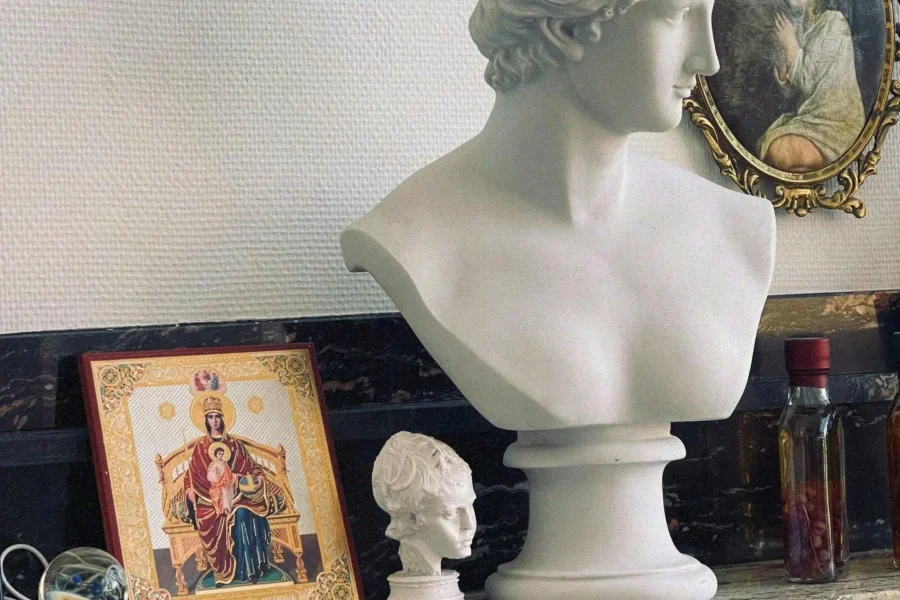 Marble bust of Venus alongside religious icon and antique mirror on ornate shelf.